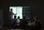 People gathered around table and man pointing to tech display